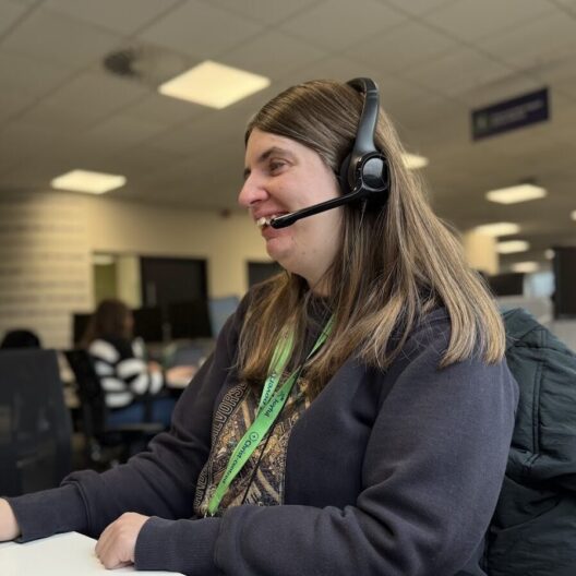 CAP worker, Amy, sat at her desk with her headset on, looking at her computer screen and smiling