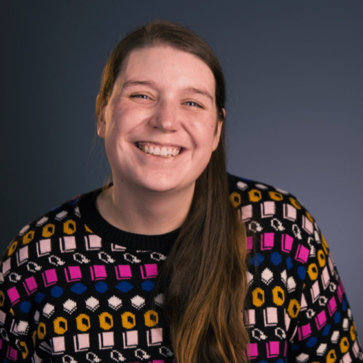 Liz Ewbank, Senior Debt Advisor, a white female with long light brown hair, a big cheesy smile, and a fun, colourful knitted jumper
