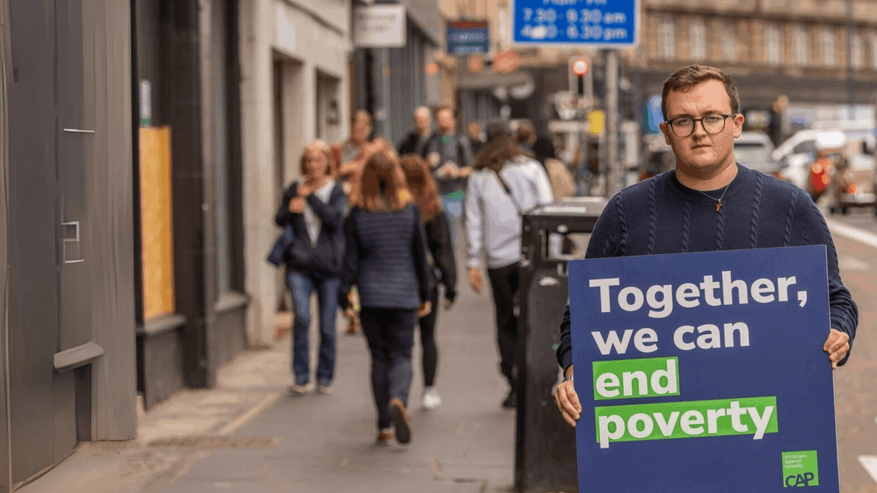 CAP Scotland staff member, Aaran, looking serious, holding a placard that reads 'Together, we can end poverty.'