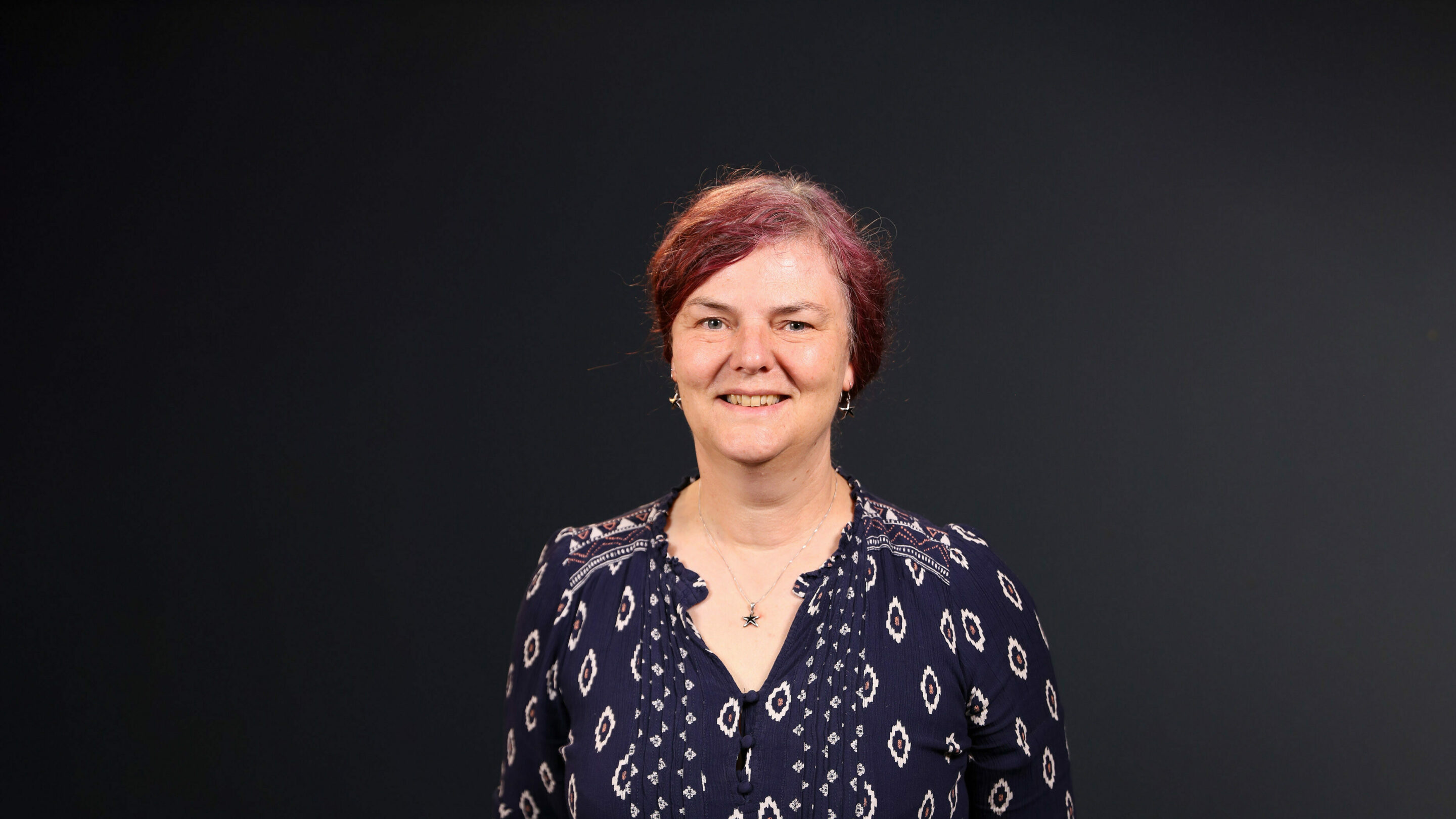 Older woman stood forwards facing the camera smiling.