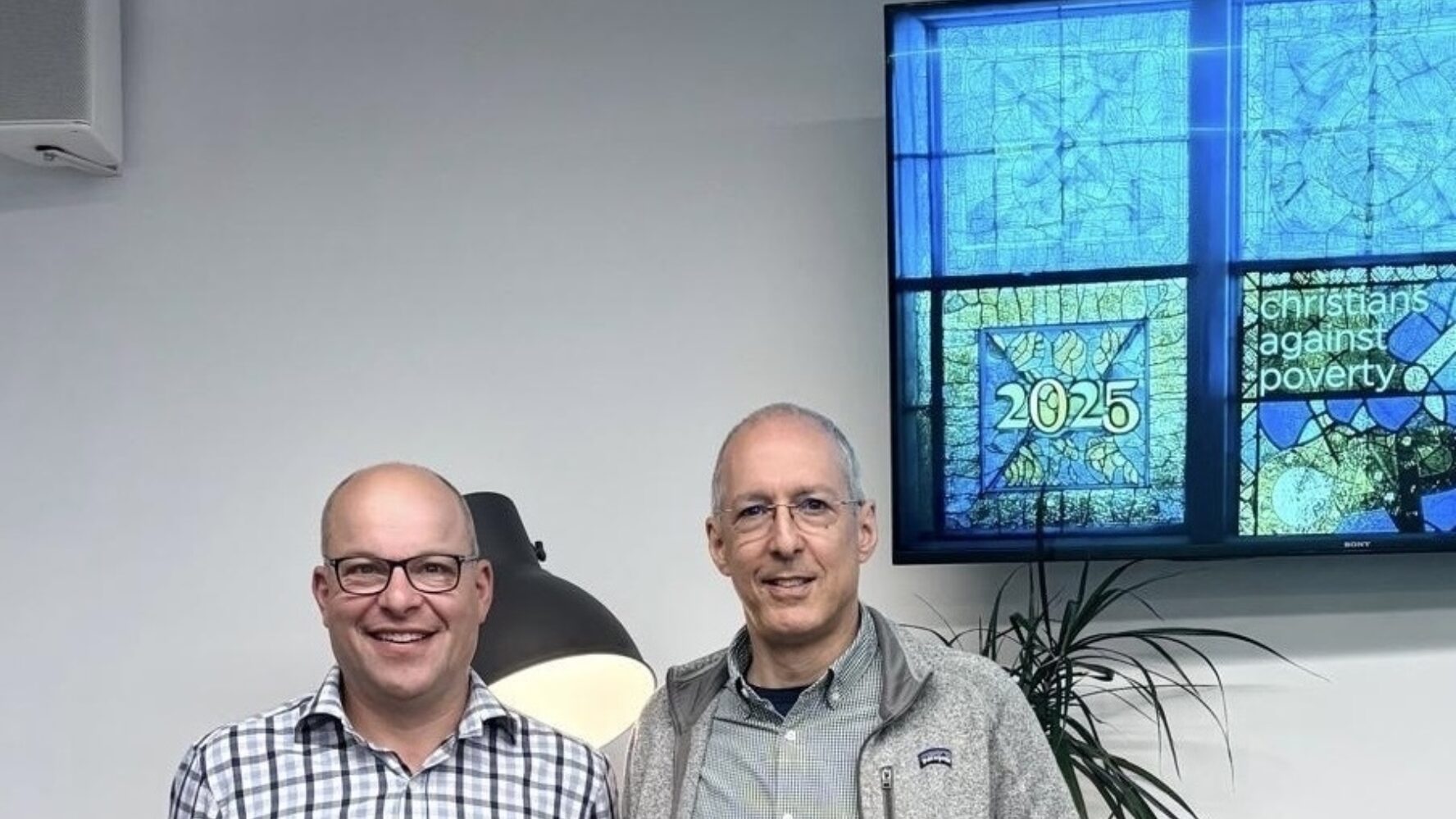 CAP's former chair of trustees, Roger Hattam, and new Chair, David Nussbaum, stand in front of a display of CAP's artwork