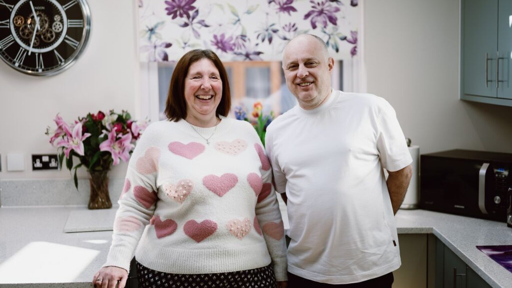 Angela, a white female with shoulder length brown hair, laughing next to her husband, a white male with no hair. He is also smiling.