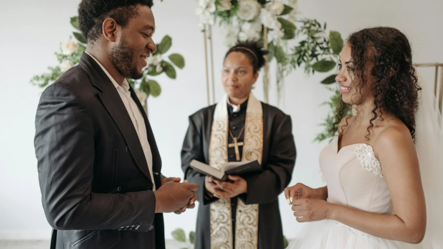 Two people stood at the altar getting married, facing each other, with the Church leader giving a bible reading for their wedding.