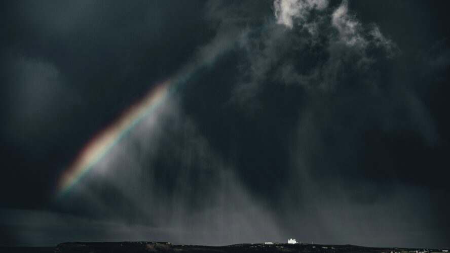 Image of a dark, stormy sky, with a rainbow coming out of the clouds on the left-hand side