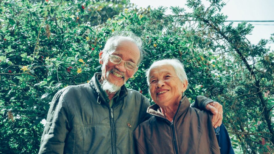 An older couple. Both of them are smiling at the camera.