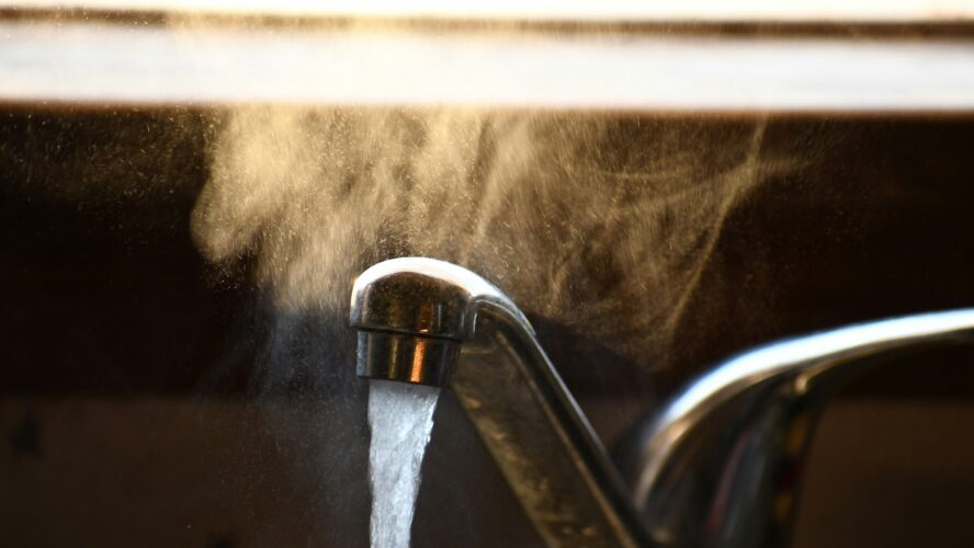 A close-up image of a tap with running water, and steam above it