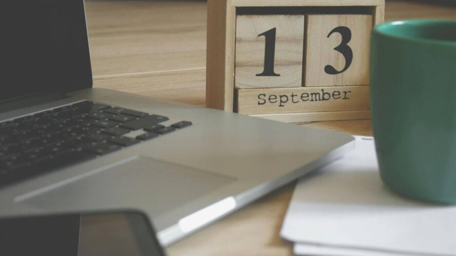 A laptop on a table next to a mug and a wooden calendar showing the date '13 September'