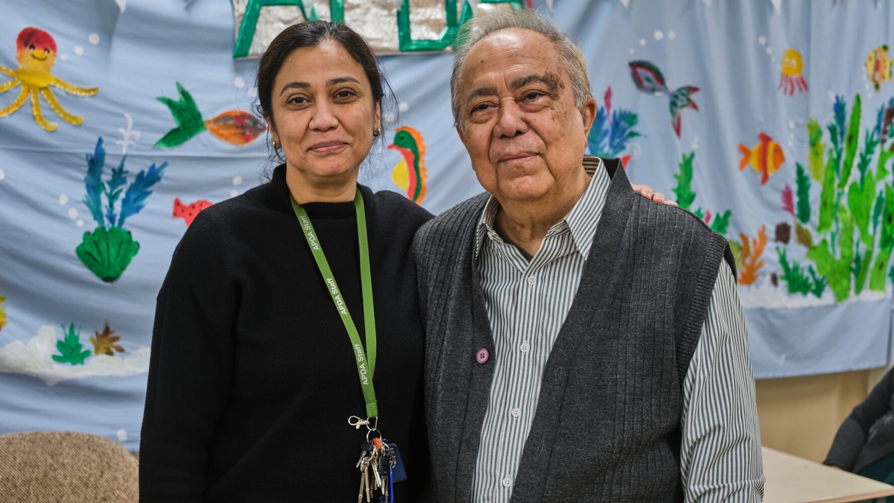 A carer with her arm around an older gentleman, smiling at the camera