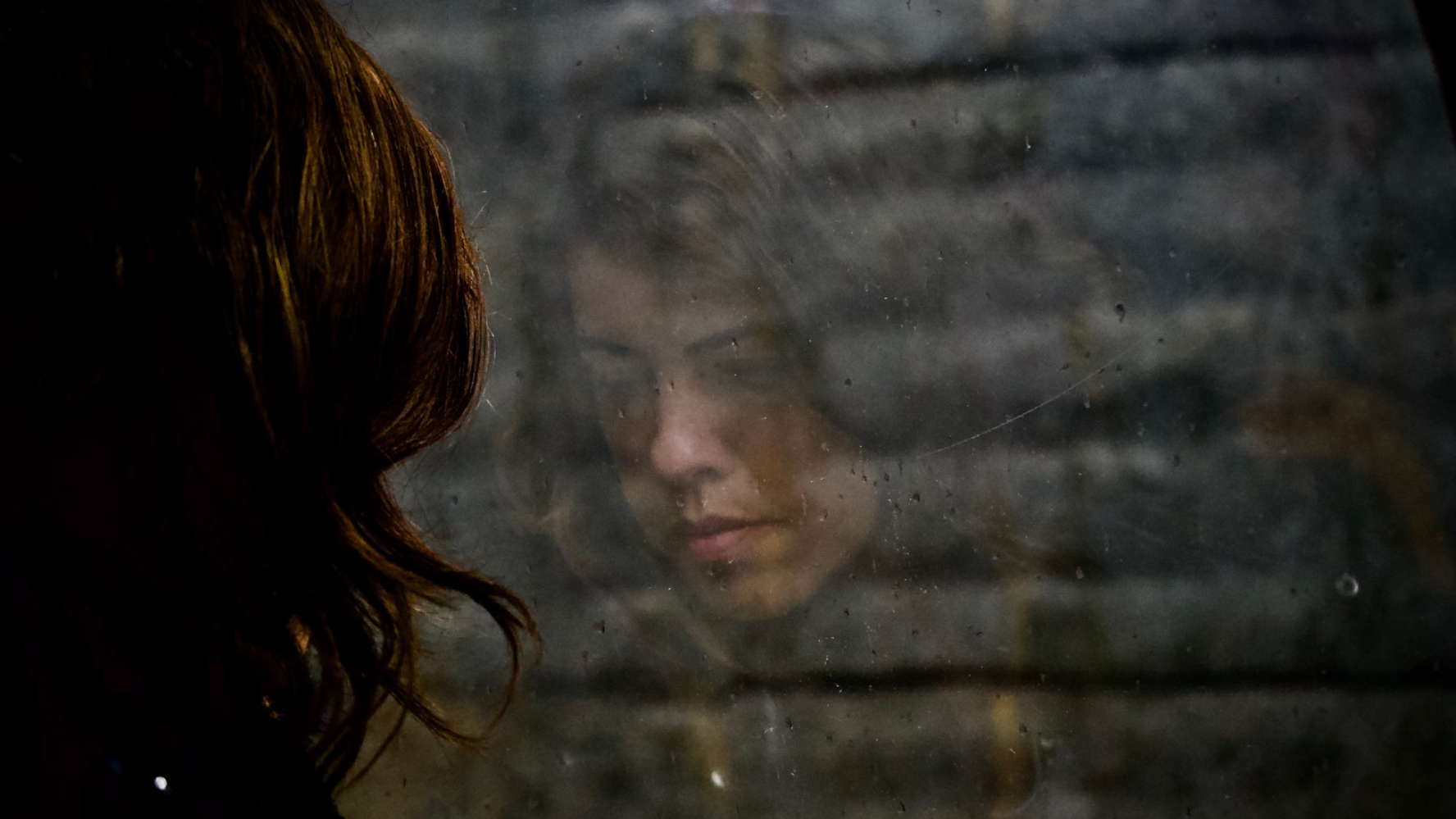 Person looking out of a window, their reflections showing a sad expression