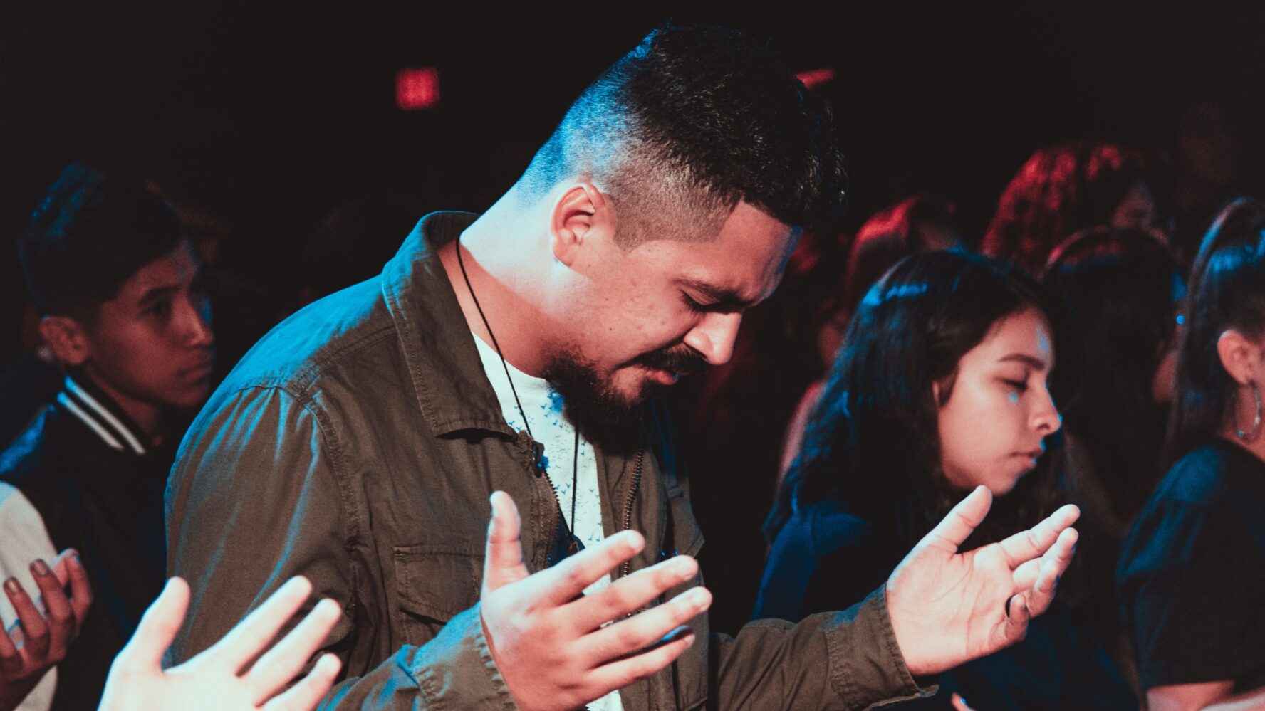 A man in his church bowing his head with his eyes closed and hands open in front of him.