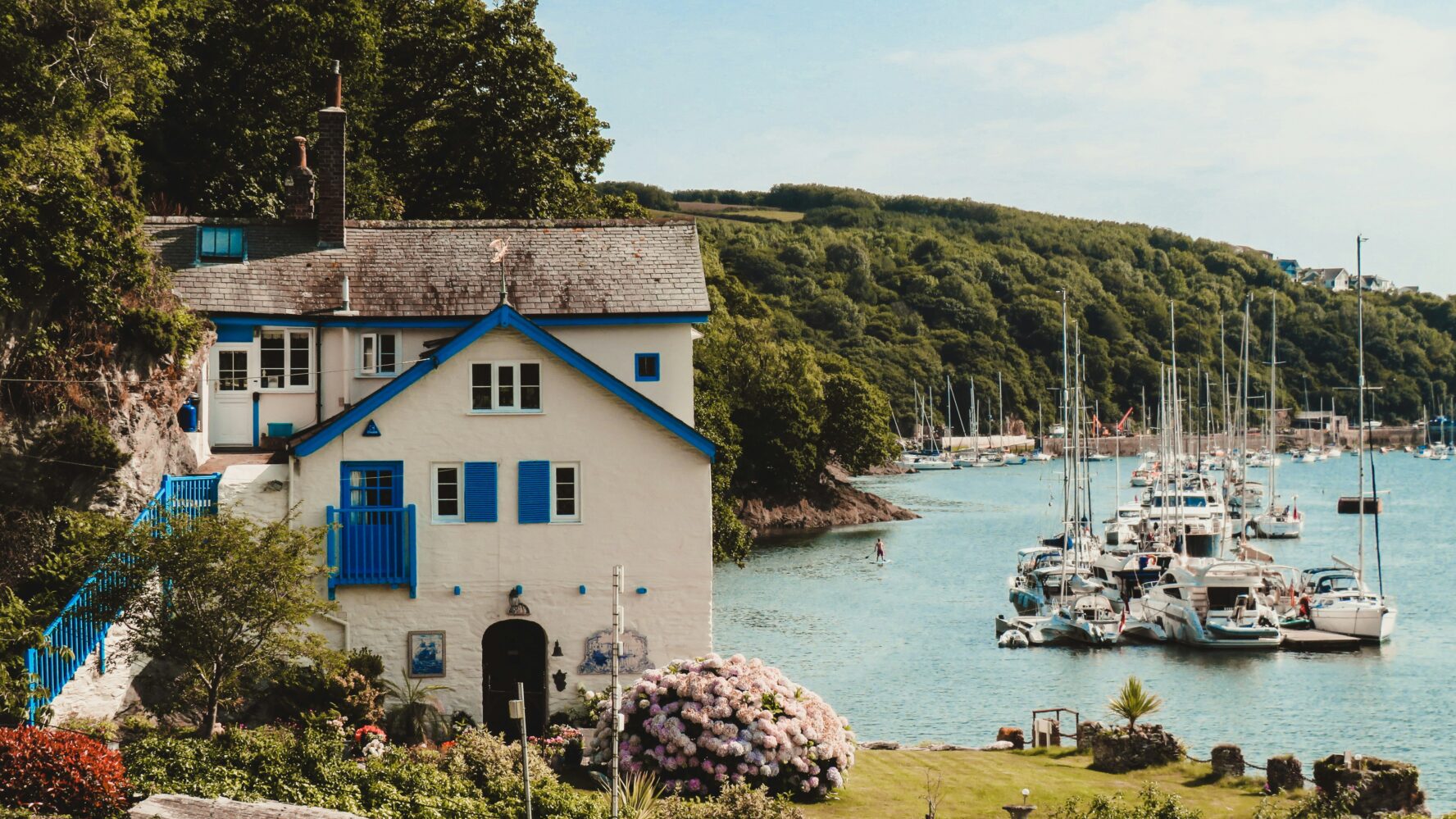 A UK coast with a white and blue building by the shore, with boats in the harbour