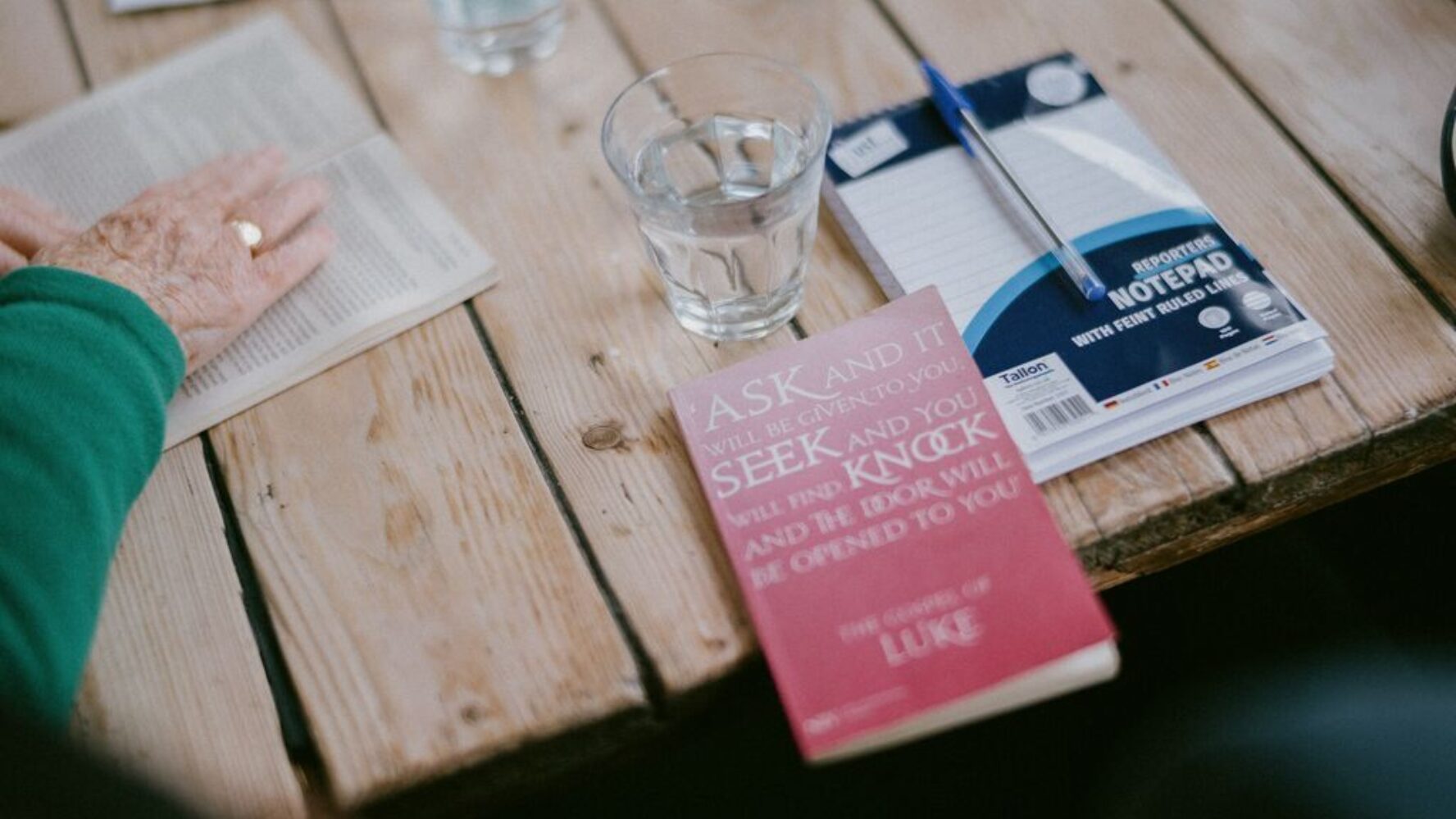 A wooden table with the book of Luke on it from the Bible, and a notepad and pen