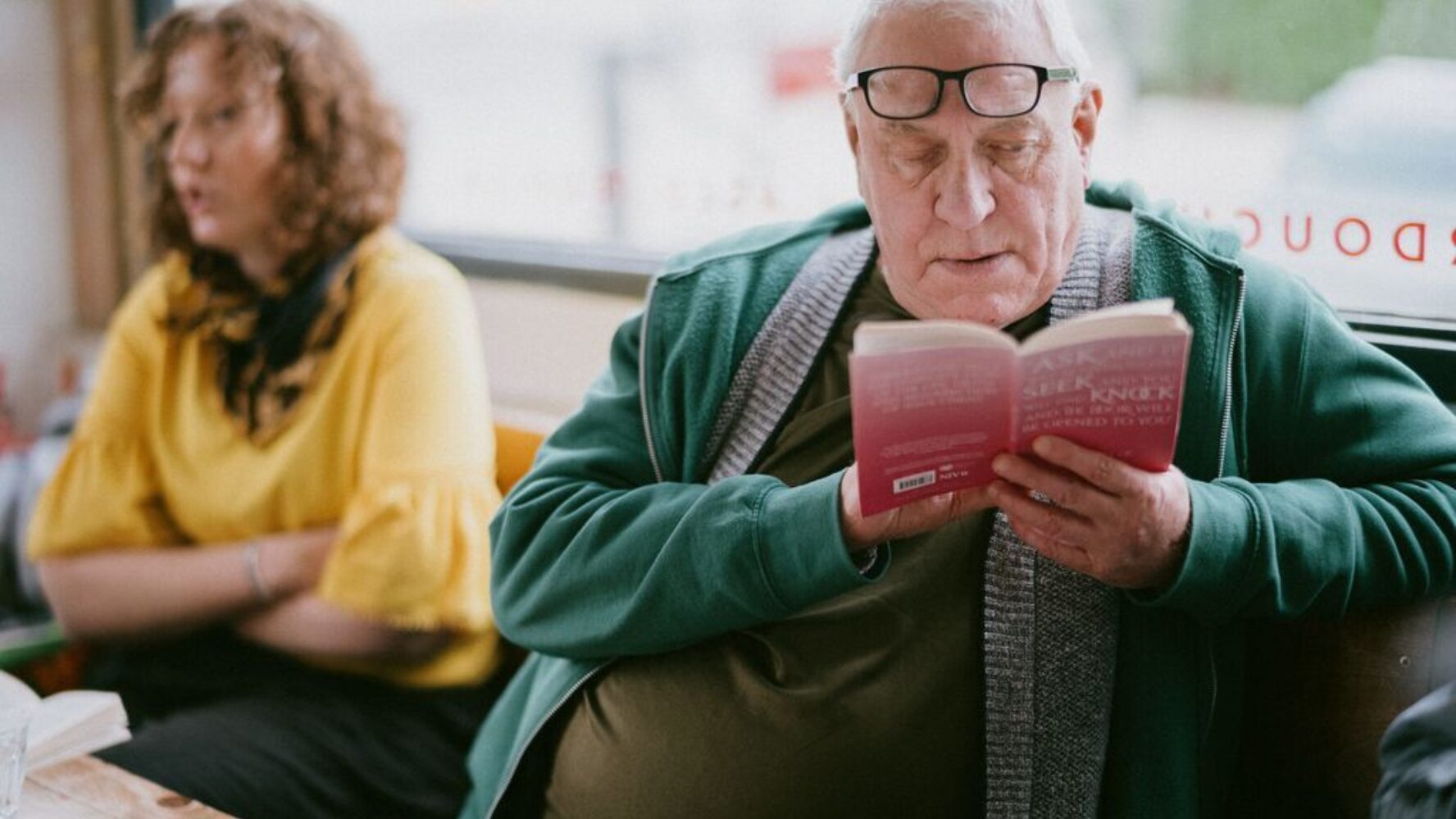 An older gentleman sat at a table at a community group, reading the bible