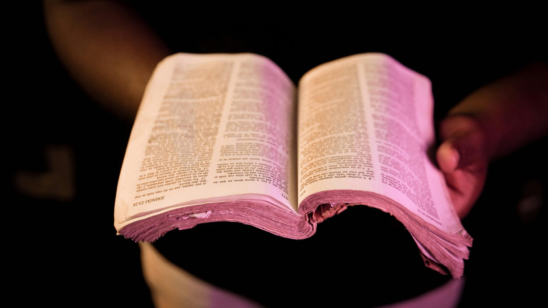 Black hands holding a well-worn Bible, open. Photography by Orlando Allo.