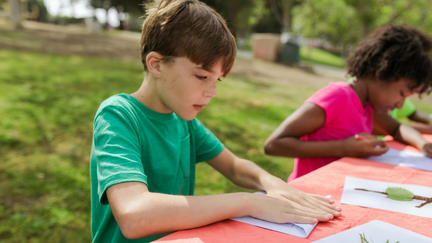 Image of a boy sat outside sticking leaves and twigs on a piece of paper to make a nature picture