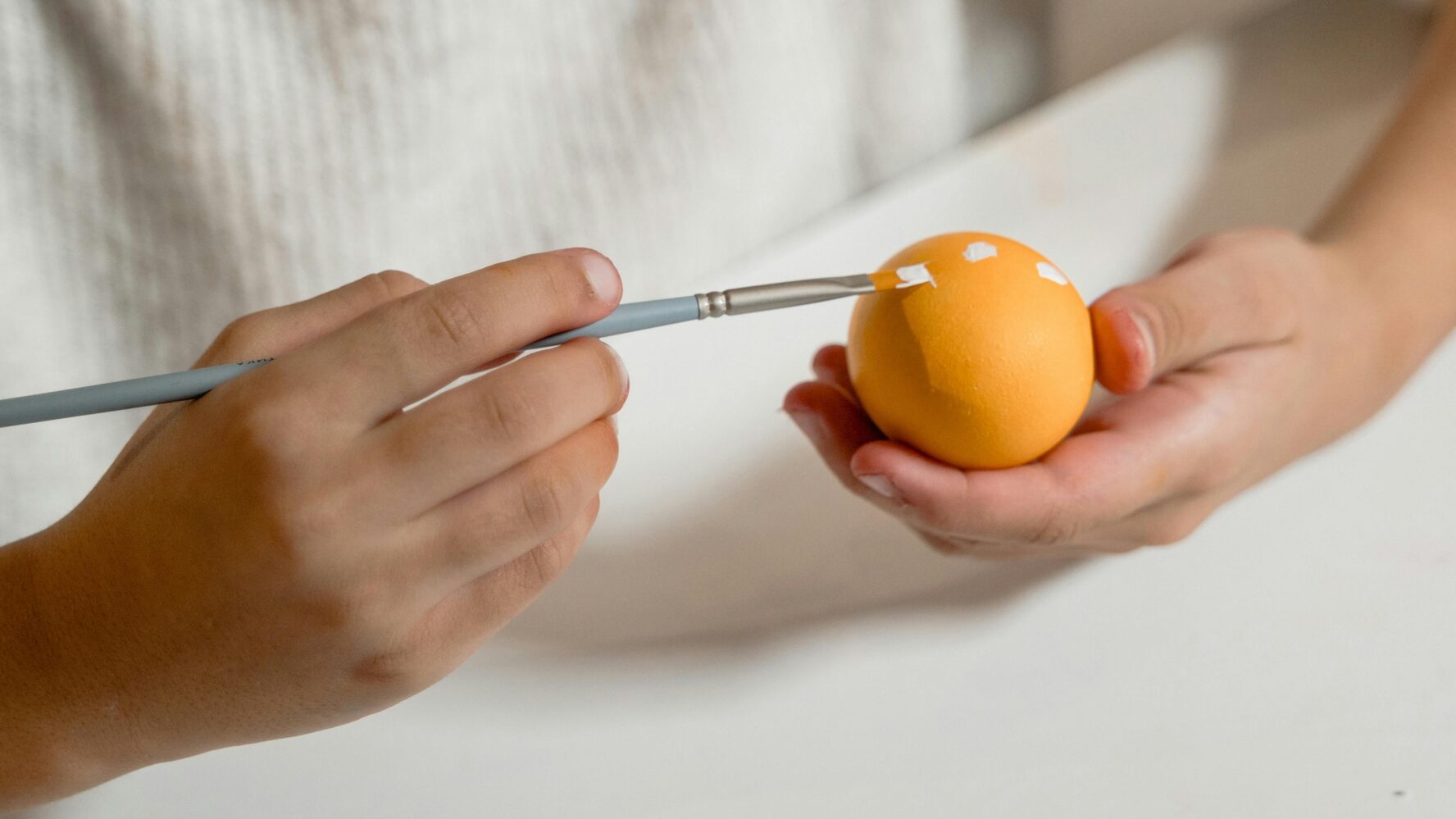 Image of a person's hands painting a hard boiled egg with paint