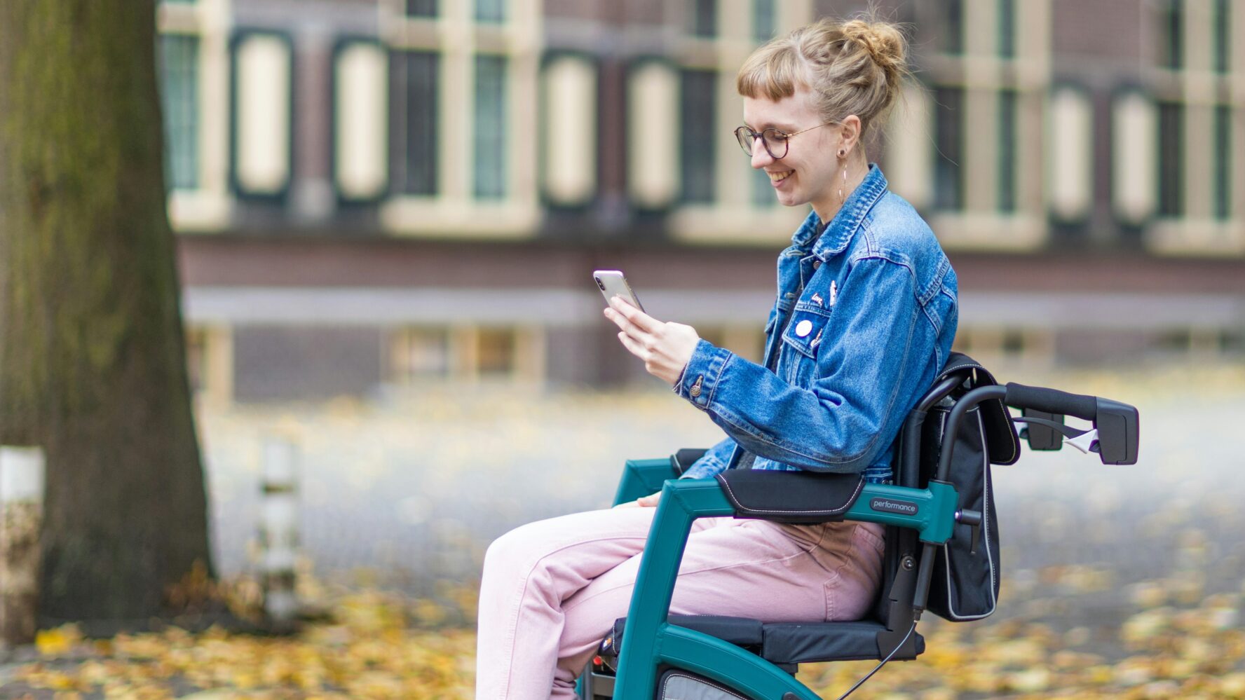 Younger lady sat in a wheelchair, holding her phone and smiling at it