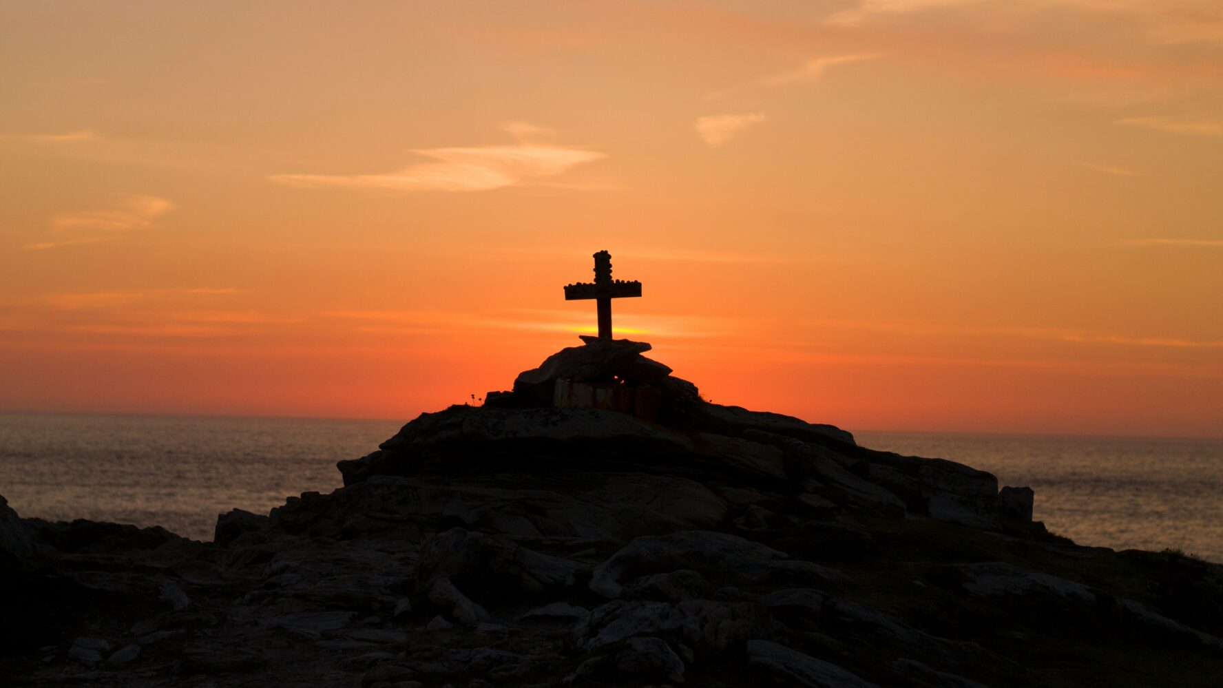A cross on a hillside, overlooking the ocean and a sunset