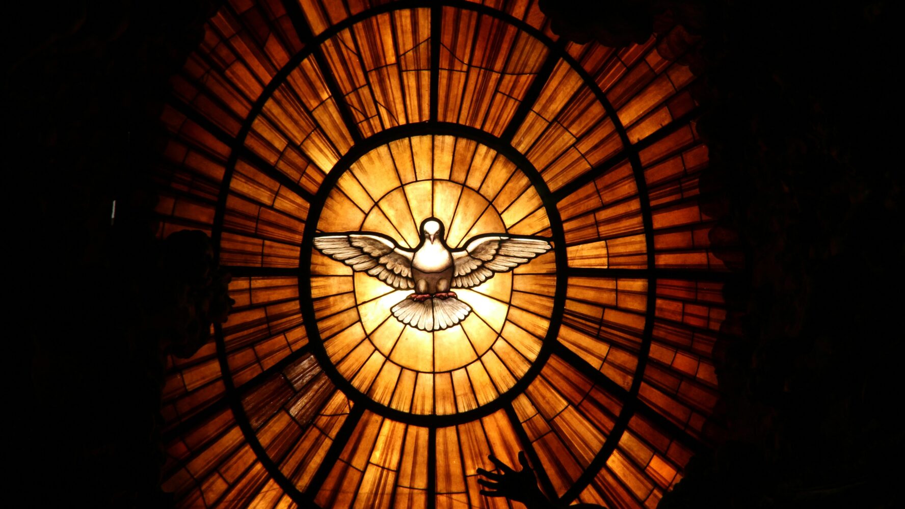 Image of a stained glass window with a dove in the middle and orange and yellow stained glass surrounding it