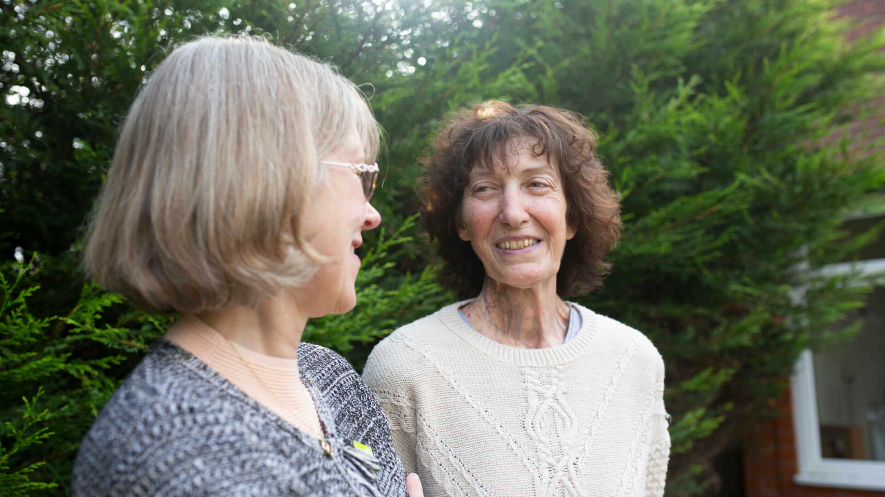 Two older women stood outside looking at each other, smiling and chatting.