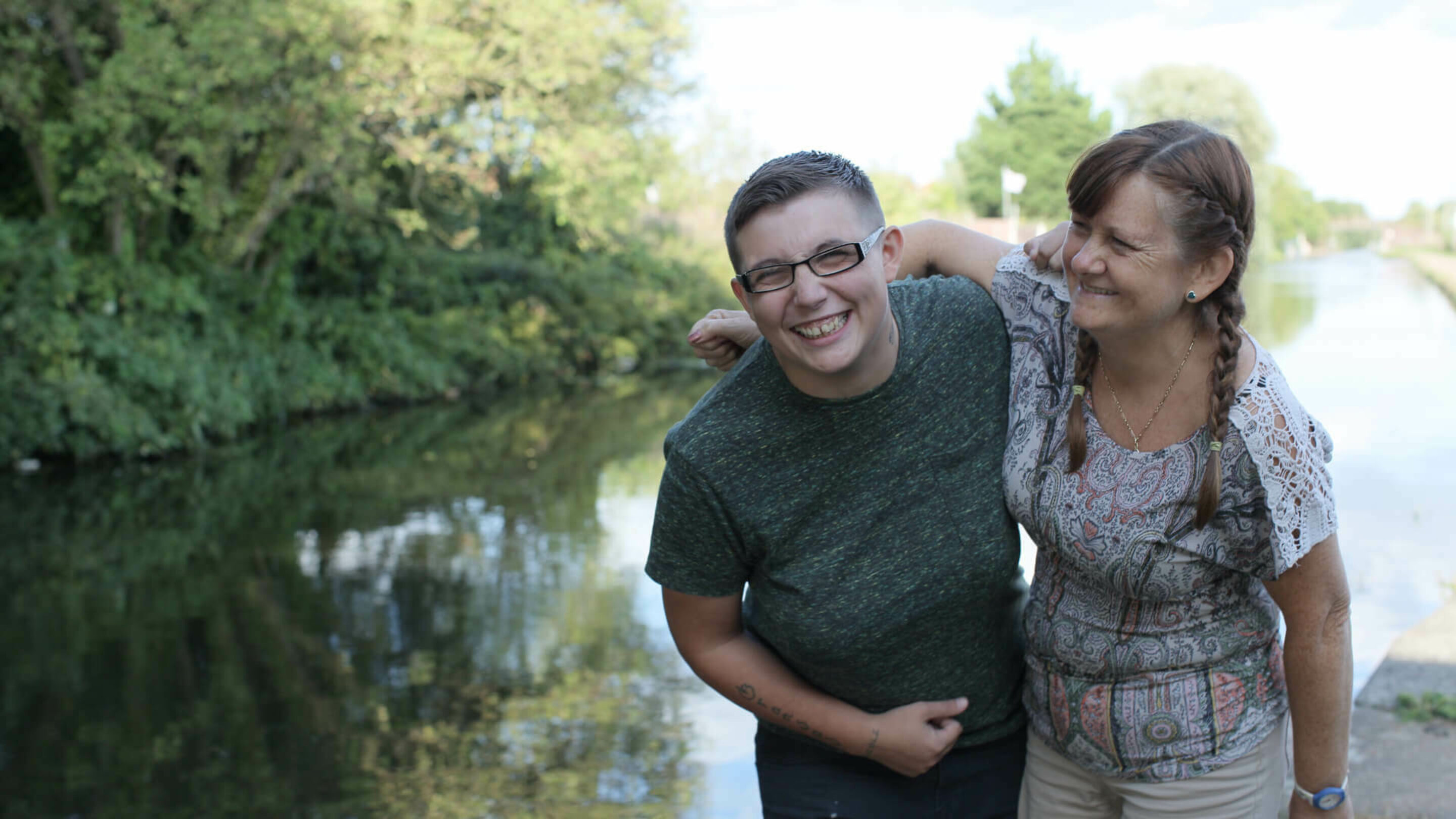 Two females with their arms around each other and laughing, walking along a canal.