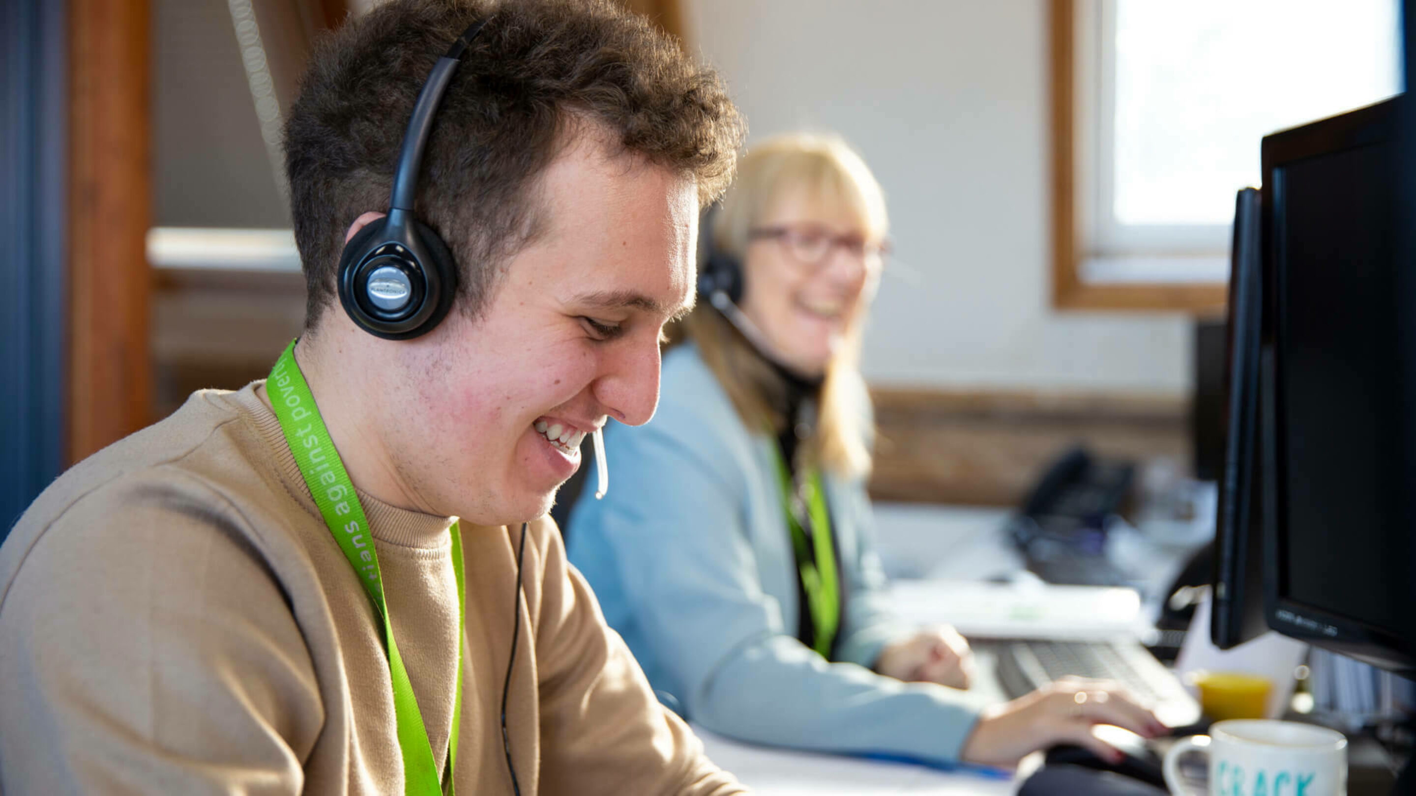 Young male wearing a phone headset and smiling as he types at his computer.