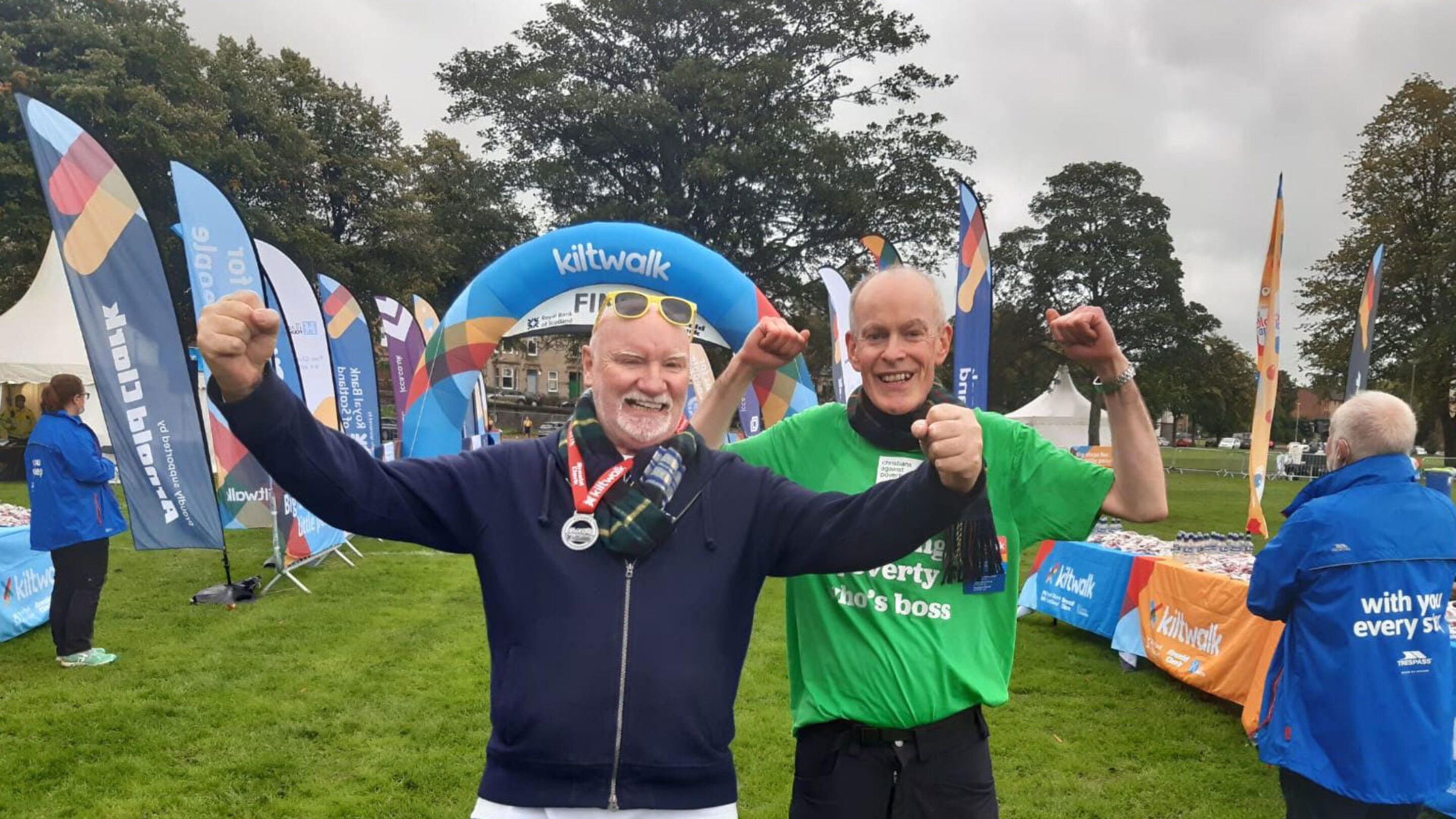Two older males stand facing the camera and cheer with their arms raised, both smiling broadly.