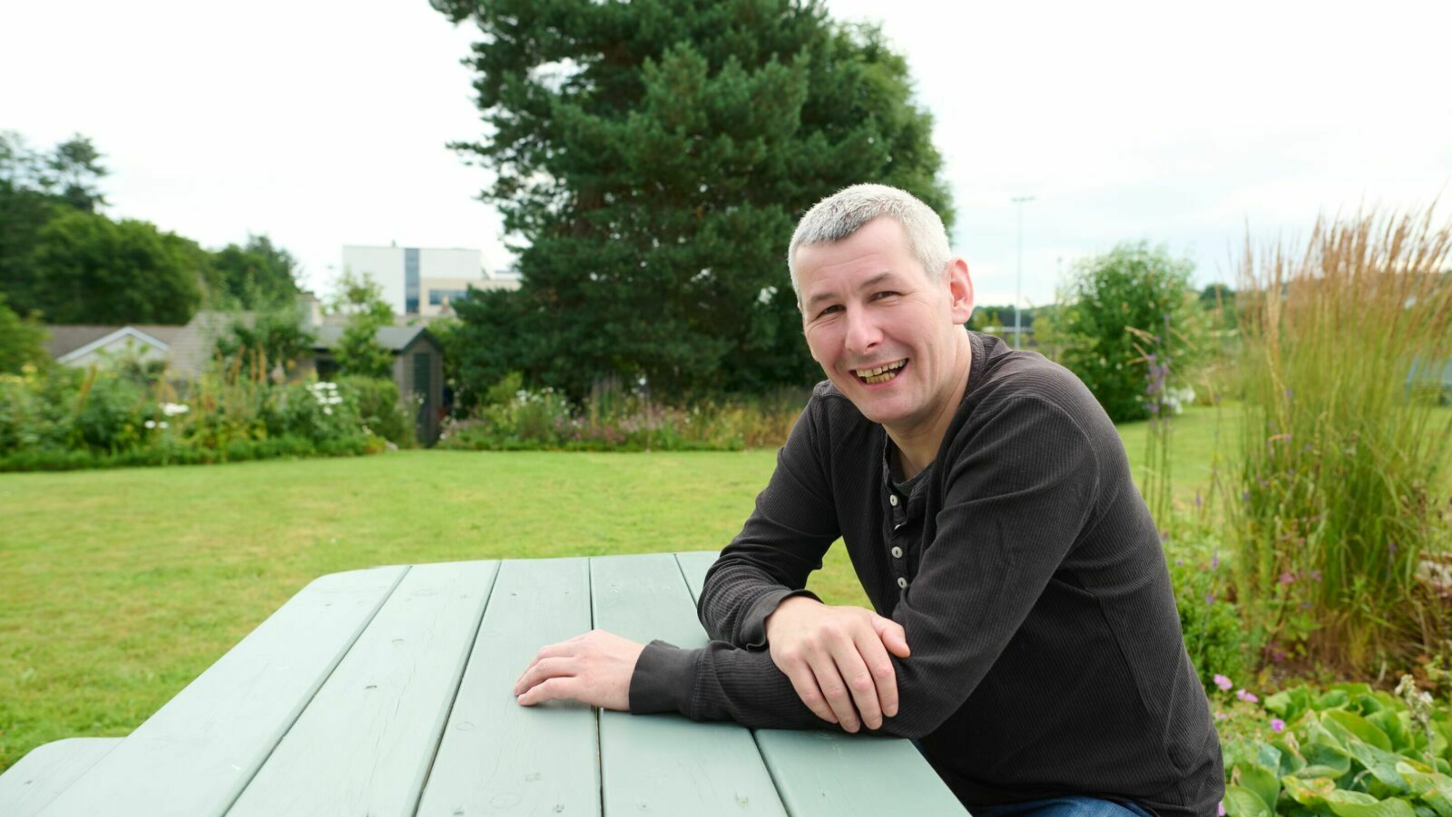 Older male sat on a bench smiling towards the camera.