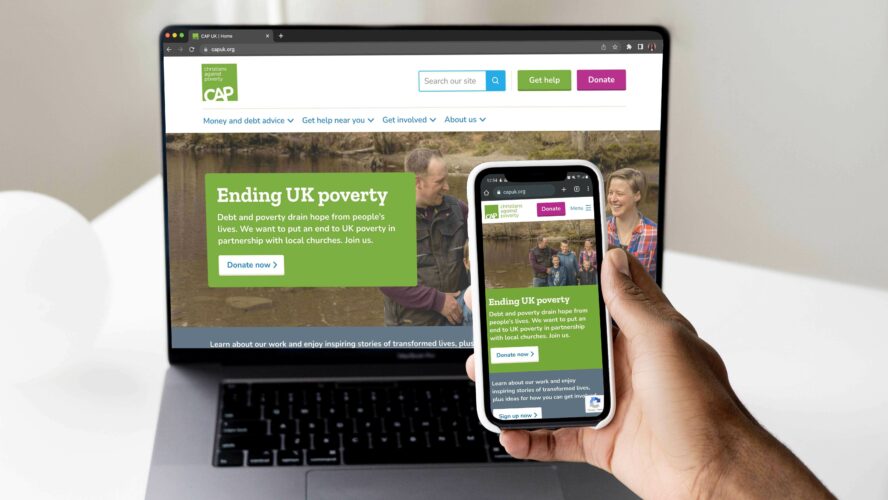 Laptop screen showing the website with a hand holding a phone with the same website screen.