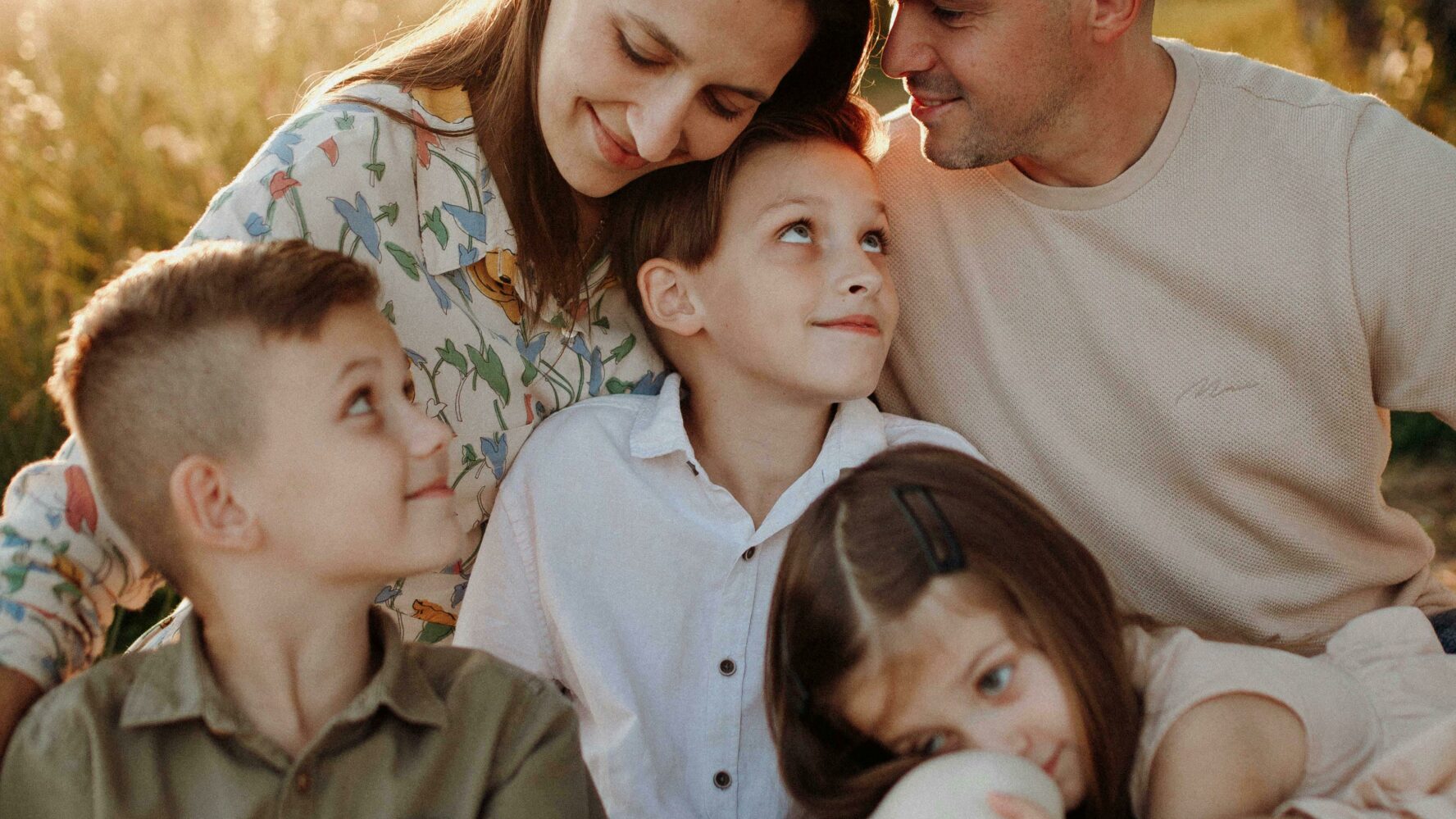 A mother, father, two sons and daughter sitting down in a park