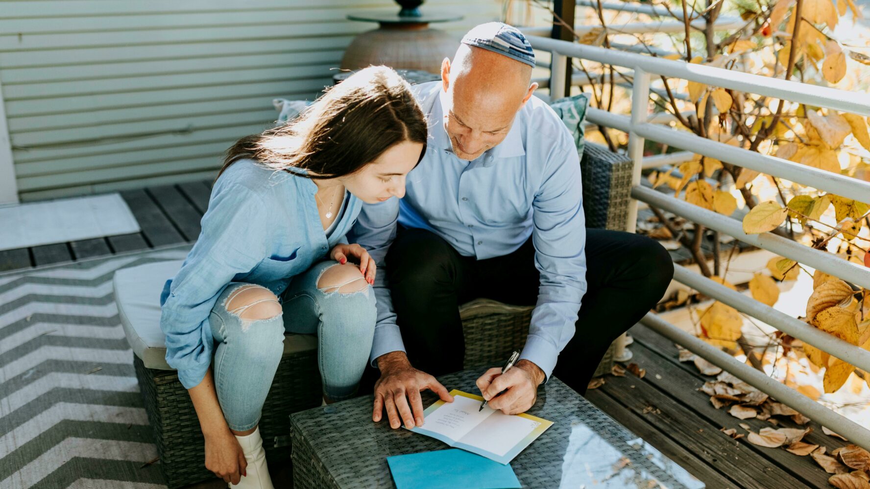 Image of a father and daughter sat outside, writing a greeting card together