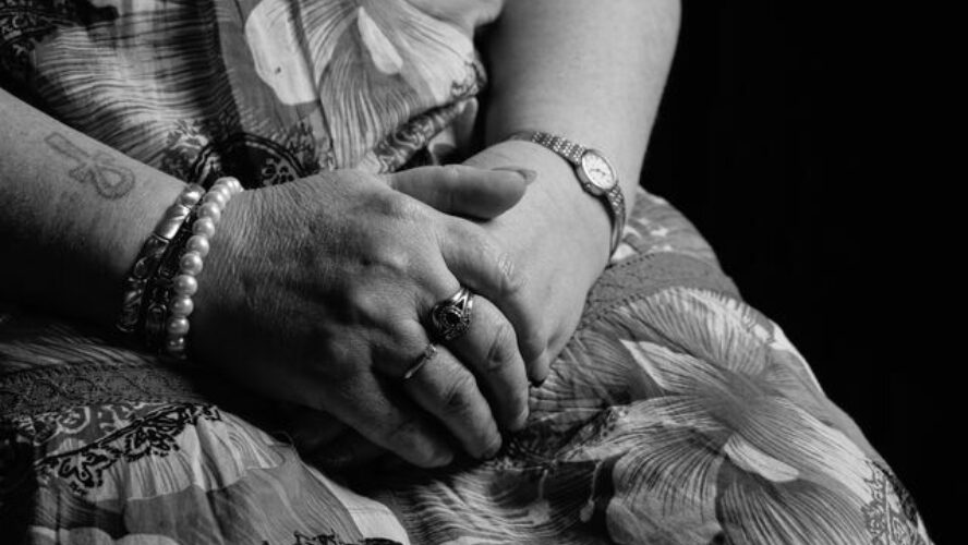 Close up black-and-white photo of a middle aged person's hands on their lap.