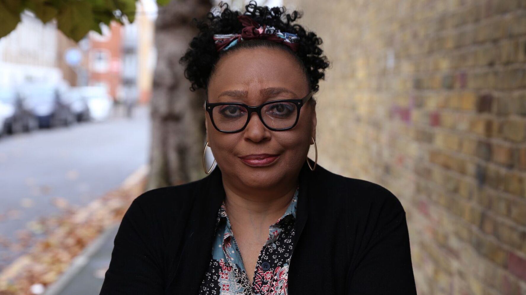 Close up shot of CAP client, Sharon, wearing glasses and a black cardigan, stood outside in her local area