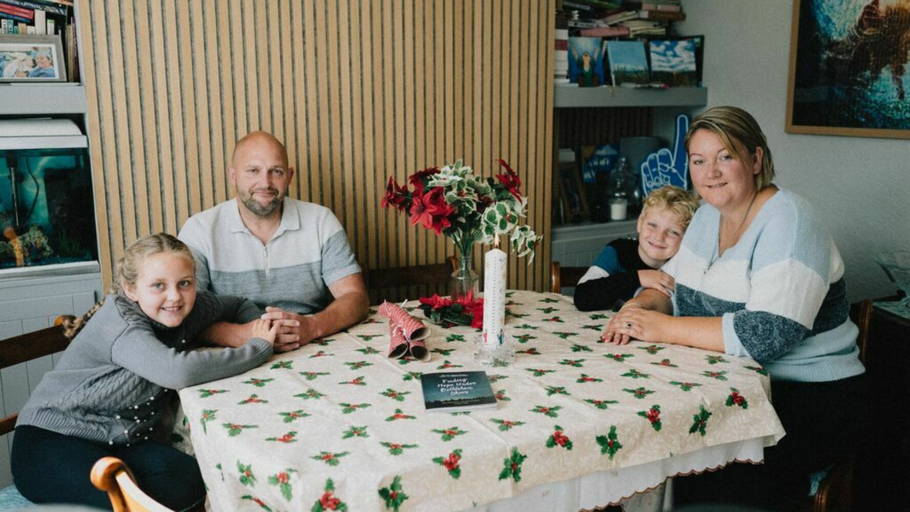 Image of a family of four - two adults and two children - sat around their dining table at Christmas, smiling at the camera