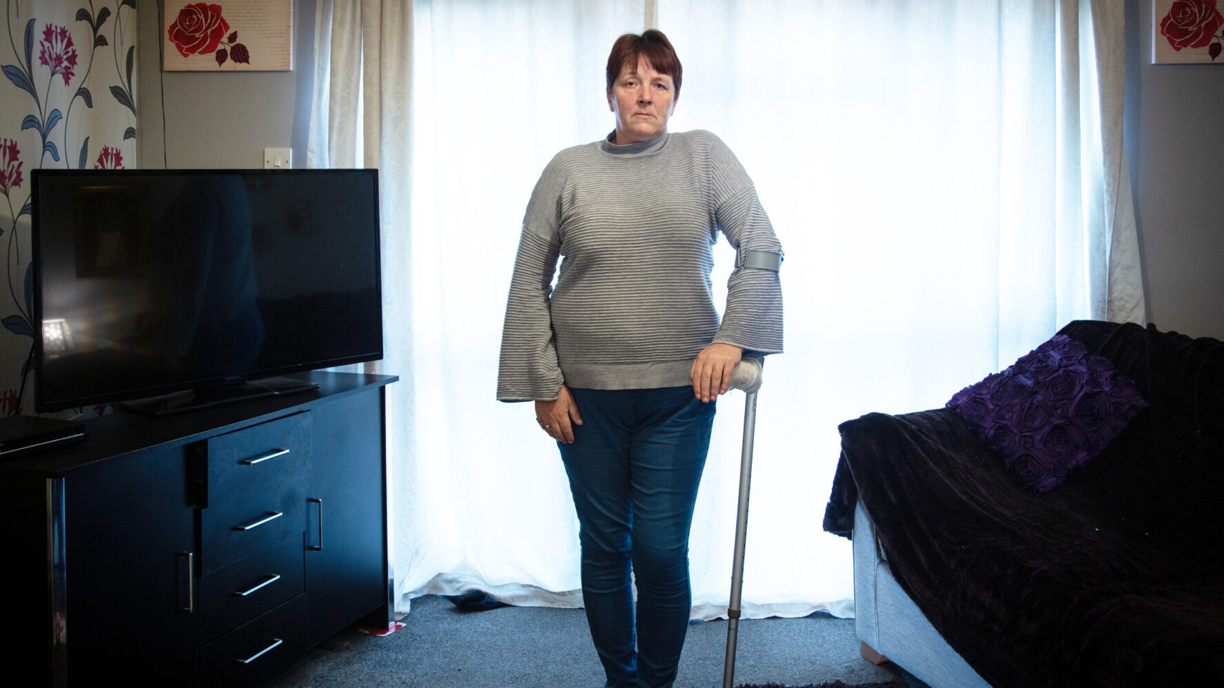 CAP client, standing in her living room using her crutch on her left arm