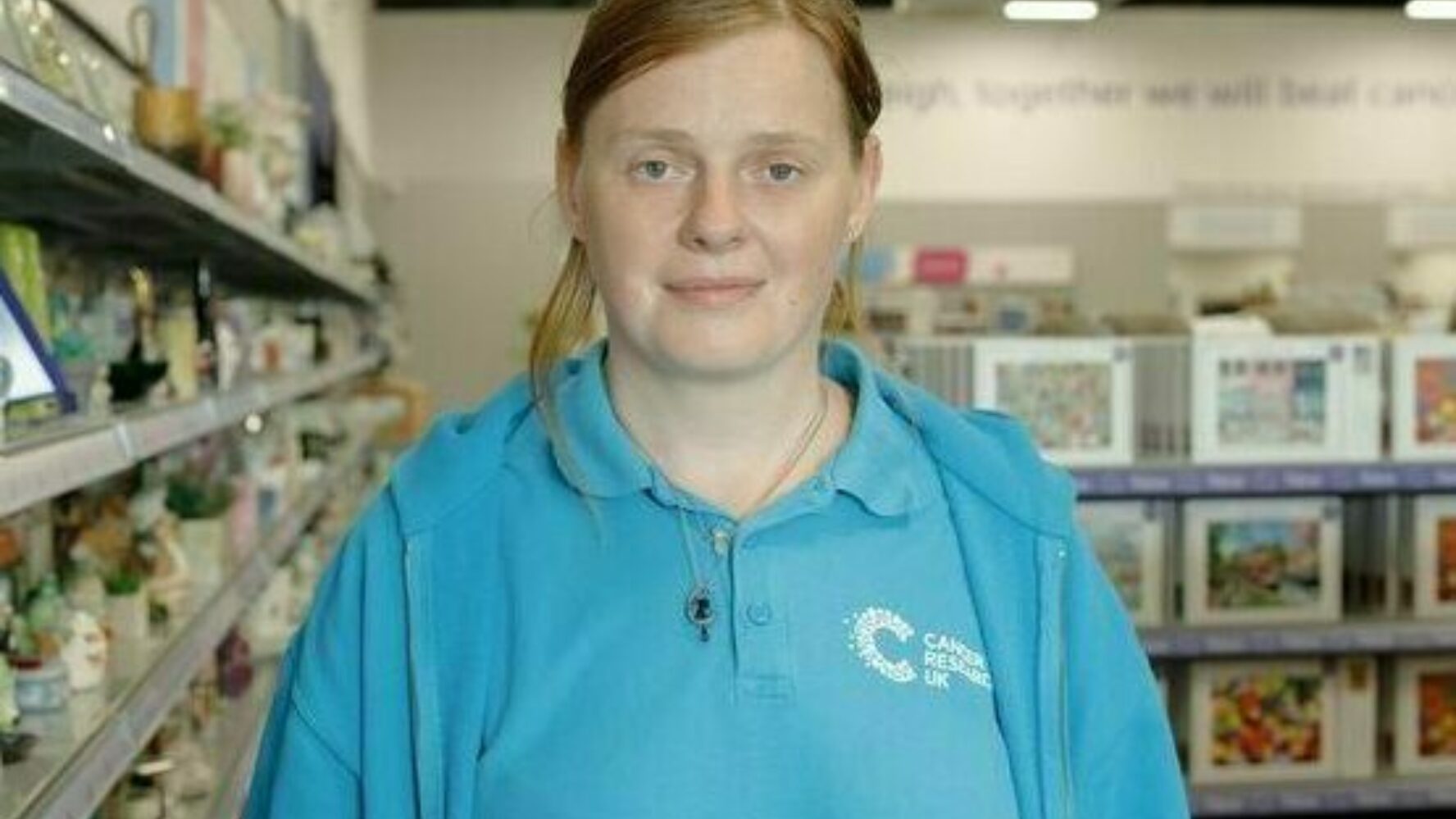 CAP client, Lyndsey, stood in a charity shop where she volunteers, smiling at the camera